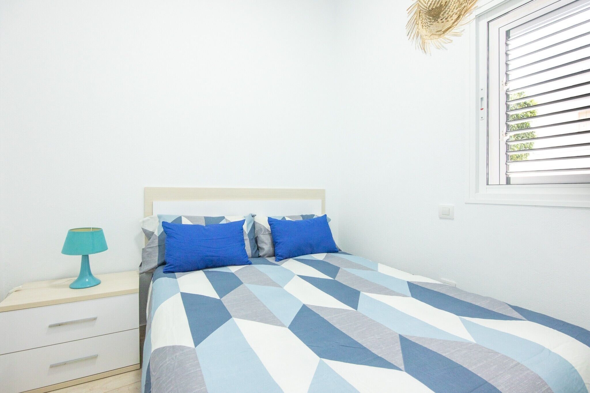 A bedroom with a bed, a nightstand, a lamp, and a window with blinds.