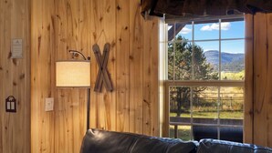 A wooden interior with a leather couch, a wall-mounted lamp, and a window offering a view of a landscape.