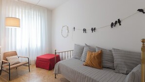 Un dormitori amb un llit, una cadira, un pouf vermell, una làmpada i decoracions murals, incloent ocells i una corona.