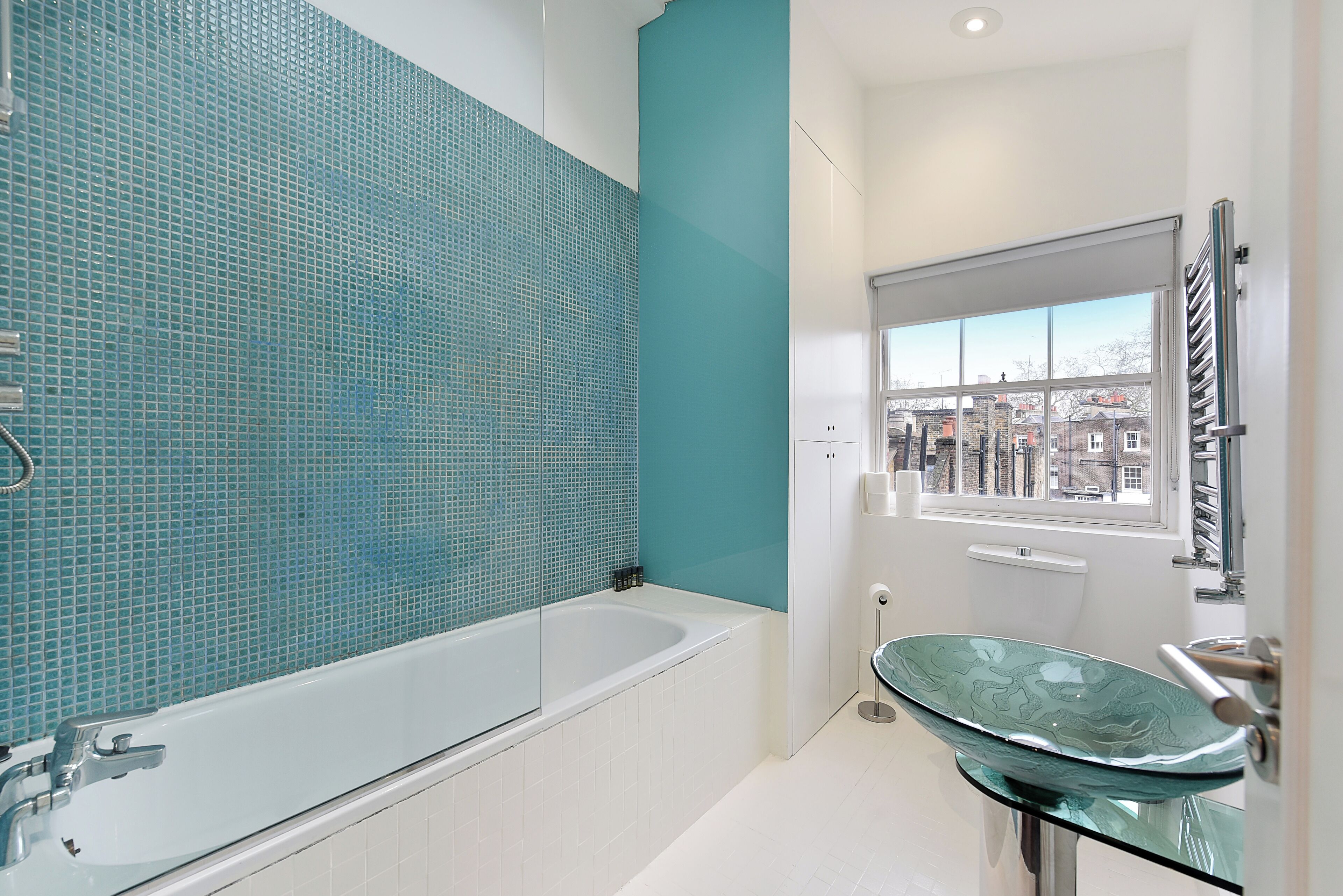 A modern bathroom with a glass sink, a bathtub, and a view of the city through a window.