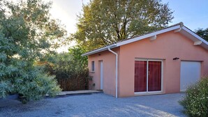 A single-story house with a garage, a gravel driveway, and a small garden area with various plants.