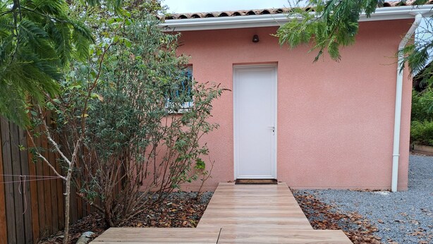 A wooden pathway leading to a pink house with a white door.