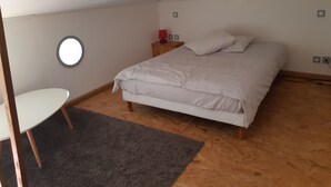 A bedroom with a bed, a round wall light, a small bedside table, and a chair.