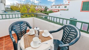 Un balcón con dos sillas, una mesa y una cafetera.