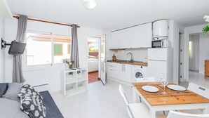 Una cocina moderna con armarios blancos, una mesa de comedor con sillas y un televisor montado en la pared.