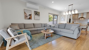 A modern living room with a grey sofa, a wooden coffee table, and a dining area with a kitchen in the background. - Anira: A Stylish New Escape in Lakes Entrance (Lakes Entrance)