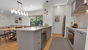 A modern kitchen with grey cabinetry, a central island, stainless steel appliances, and pendant lighting. - Anira: A Stylish New Escape in Lakes Entrance (Lakes Entrance)