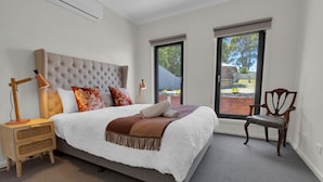A bedroom with a large bed, a nightstand, a chair, and a view of the outdoors through a window. - Anira: A Stylish New Escape in Lakes Entrance (Lakes Entrance)