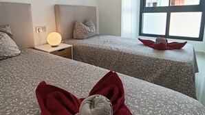 A hotel room with two beds, a bedside table with a lamp, a window with a view of buildings, and a towel on the bed. - Modern Apartment "R-60-B" in Torrevieja (Torrevieja)