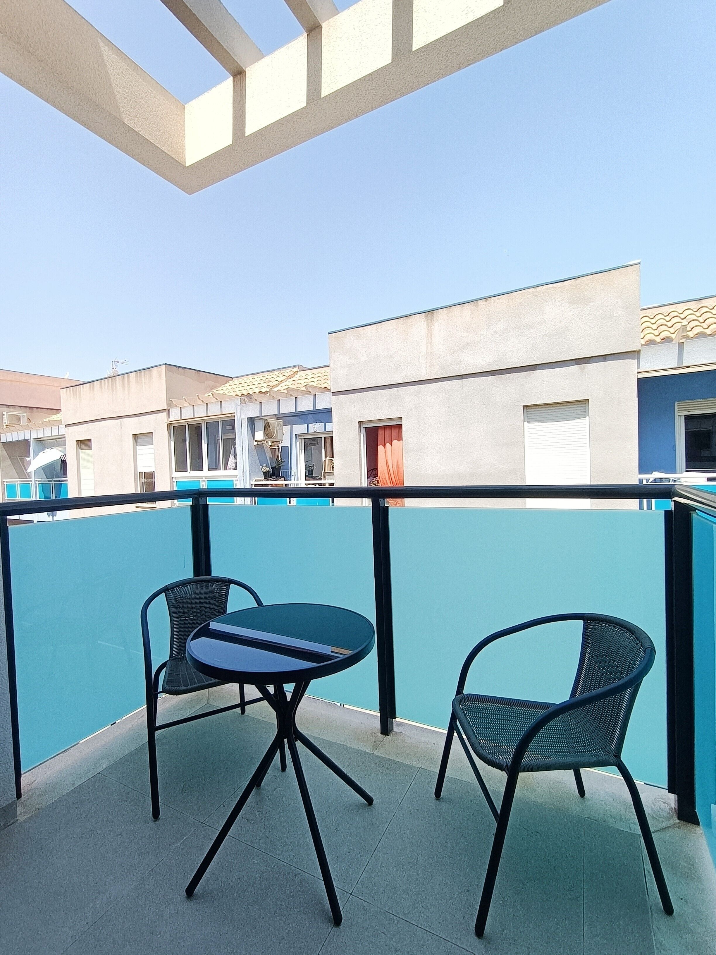 Un balcón con dos sillas y una mesa, con vista a un edificio de fachada azul y tejado de tejas.