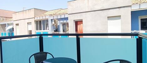 Un balcón con dos sillas y una mesa, con vista a un edificio de fachada azul y tejado de tejas.