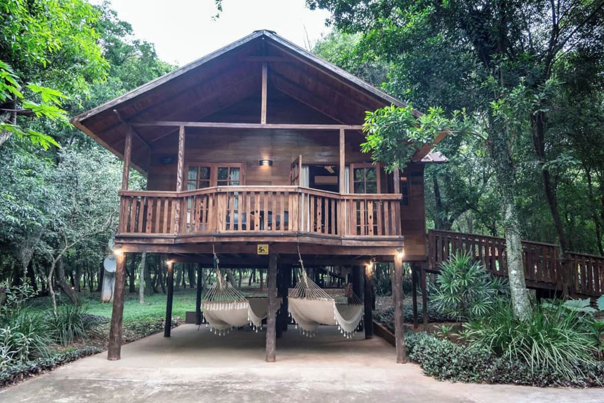 A wooden cabin with a balcony, surrounded by lush greenery.