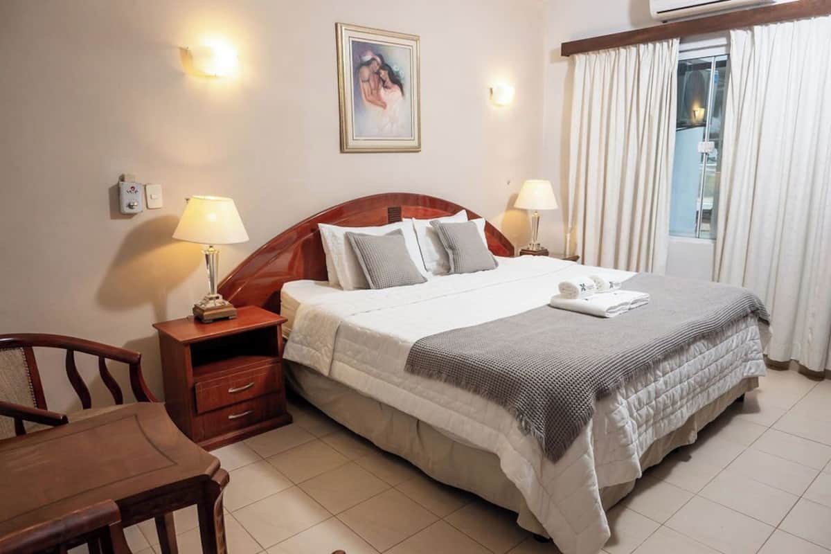 A hotel room with a bed, bedside tables, a chair, and a window with curtains.