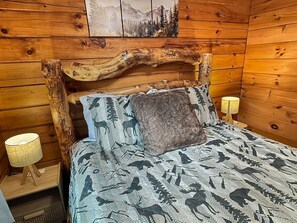 A wooden cabin room with a bed, two wall-mounted lamps, and a painting above the bed. - Cozy 2BR cabin with mountain views, WiFi, grill, and pool table. Free rafting, train, zip line tix (Bryson City)
