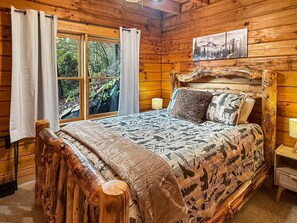 Een houten slaapkamer met een bed, gordijnen, een raam en een schilderij aan de muur.