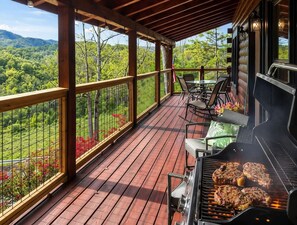 Una terrassa a l'aire lliure amb una barbacoa, cadires i vista a un paisatge forestal.