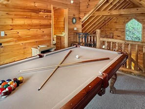 Een pooltafel in een houten kamer, met een klok en een raam.