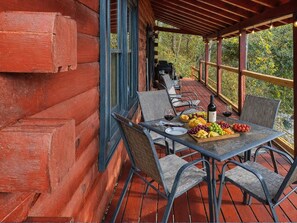 A wooden deck with a table set for dining, featuring a bottle of wine, a glass, and a fruit platter. - Cozy 2BR cabin with mountain views, WiFi, grill, and pool table. Free rafting, train, zip line tix (Bryson City)