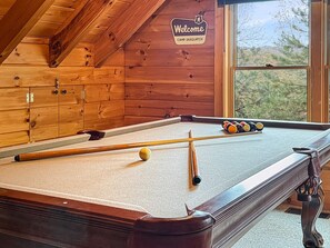 A pool table in a cabin with a 'Welcome CAMP SASQUATCH' sign, wooden walls, and a window view. - Cozy 2BR cabin with mountain views, WiFi, grill, and pool table. Free rafting, train, zip line tix (Bryson City)