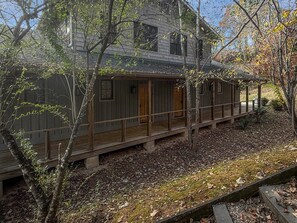 Une cabane en bois dotée d’un porche couvert, entourée d’arbres et d’un sol recouvert de feuilles.