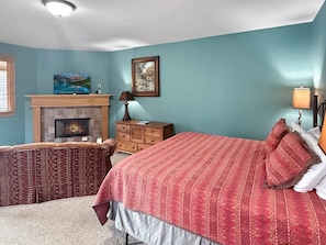 Ein Schlafzimmer mit Kamin, einem Bett mit roter Bettwäsche, einem Schminktisch und einem Gemälde an der Wand.