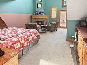Ein Schlafzimmer mit einem Bett, zwei Sesseln, einem Kamin, einem kleinen Tisch und einer Kommode.