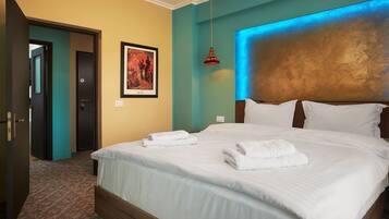 A neatly made bed with white linens and towels, a teal accent wall, and a framed picture on the wall.