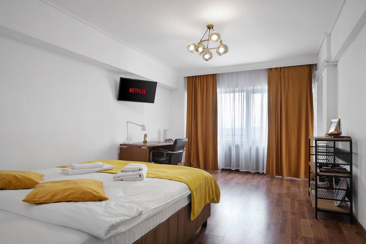 A hotel room with a bed, a desk, a chair, a TV, and a window with curtains.