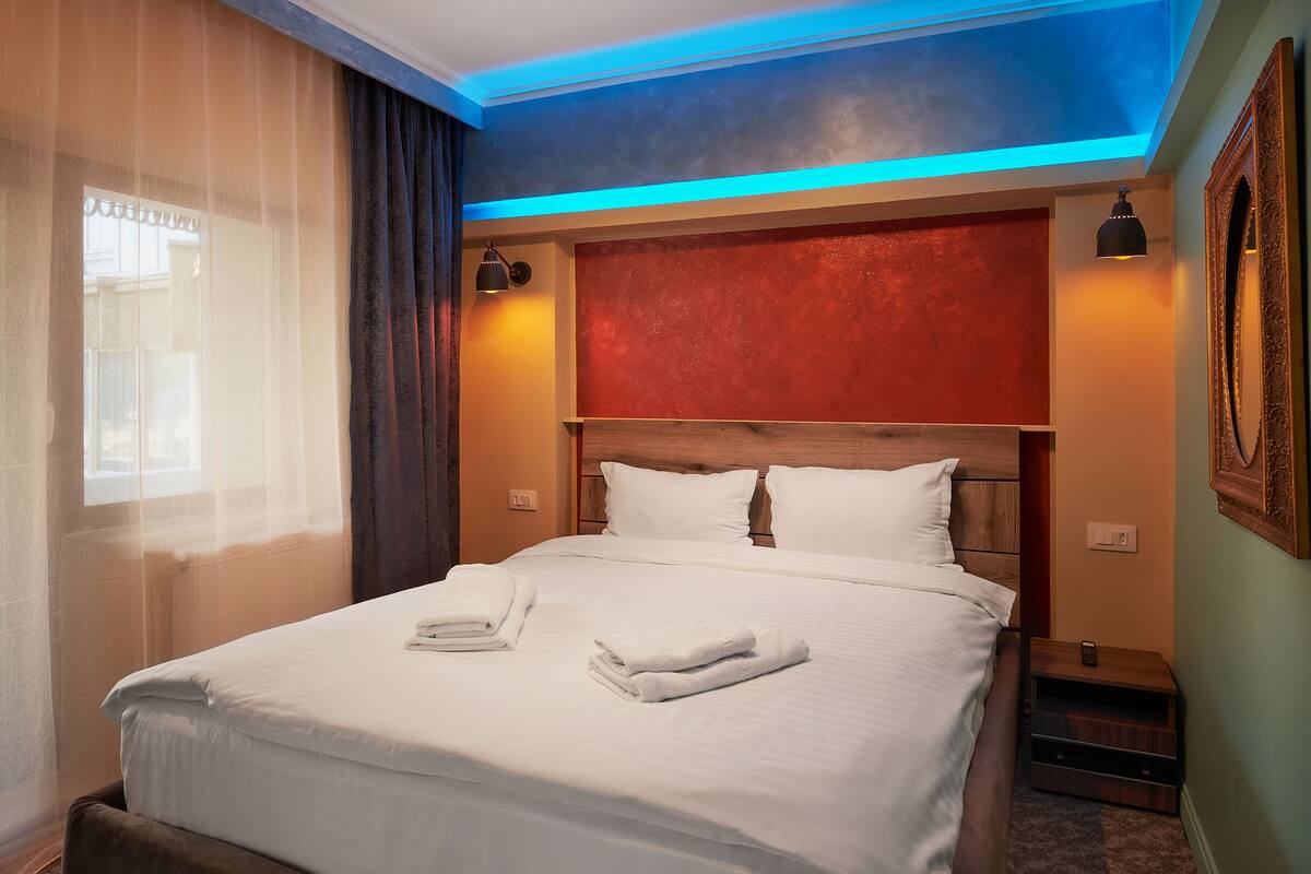 A neatly made bed with white linens and towels, a wooden headboard, and a red accent wall.