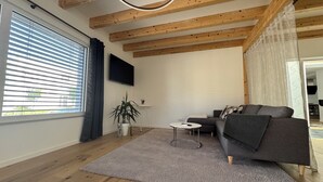 Una sala de estar moderna con vigas de madera, un sofá gris, una mesita y una planta en maceta.