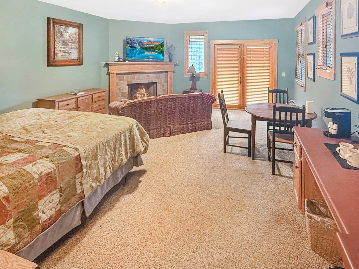 Quarto com cama, lareira, televisão e área de jantar com cadeiras e mesa.