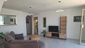 A modern living room with a grey sofa, a wooden coffee table, a TV on a wooden stand, and a potted plant. - Steps Away from the Sea- Beach Front Free Parking! (San Pawl il-Baħar)