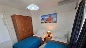 A hotel room with two beds, a wooden wardrobe, a painting on the wall, and a ceiling light fixture. - Steps Away from the Sea- Beach Front Free Parking! (San Pawl il-Baħar)