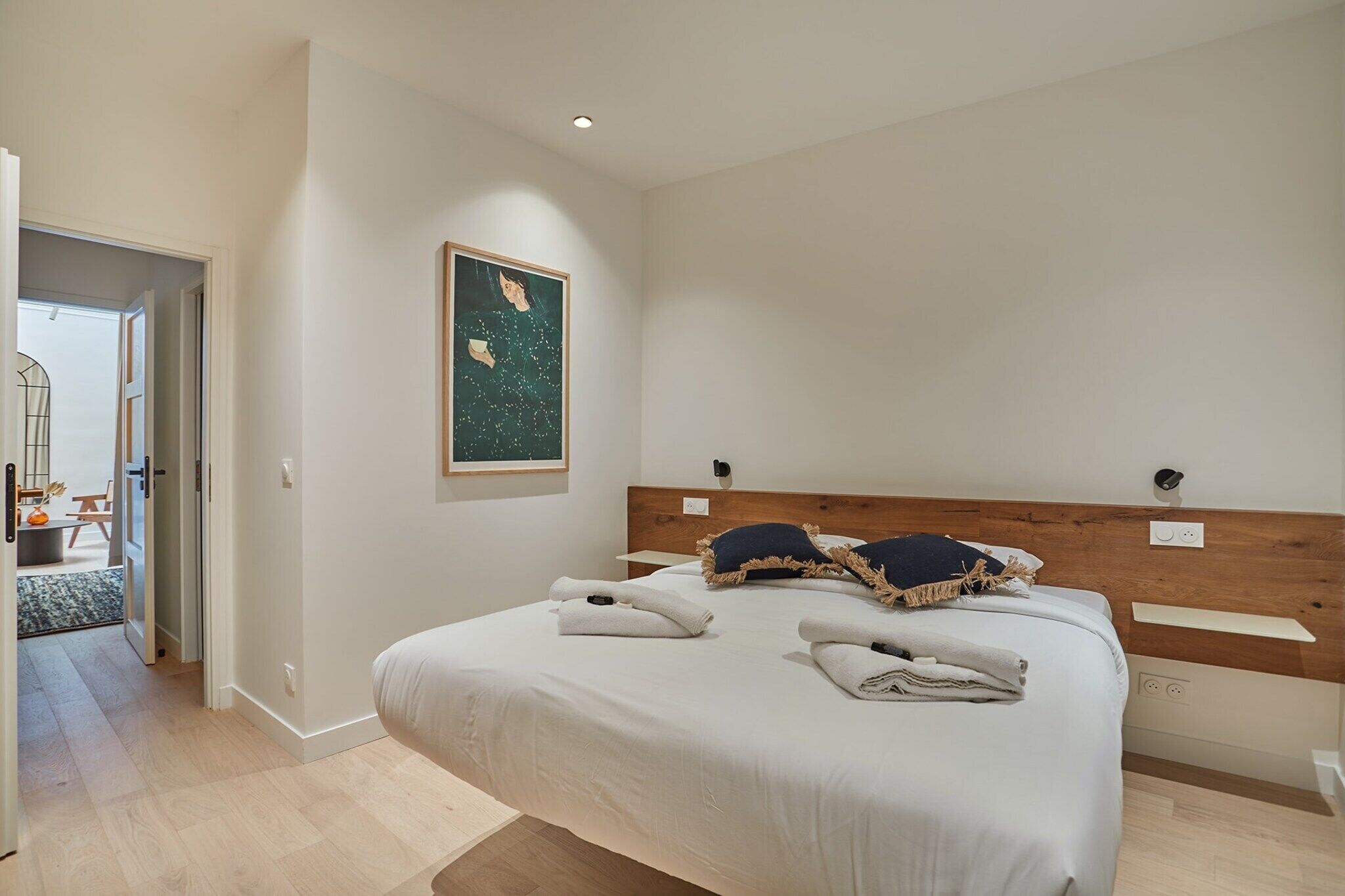 A modern bedroom with a large bed, a wooden headboard, and a painting on the wall.