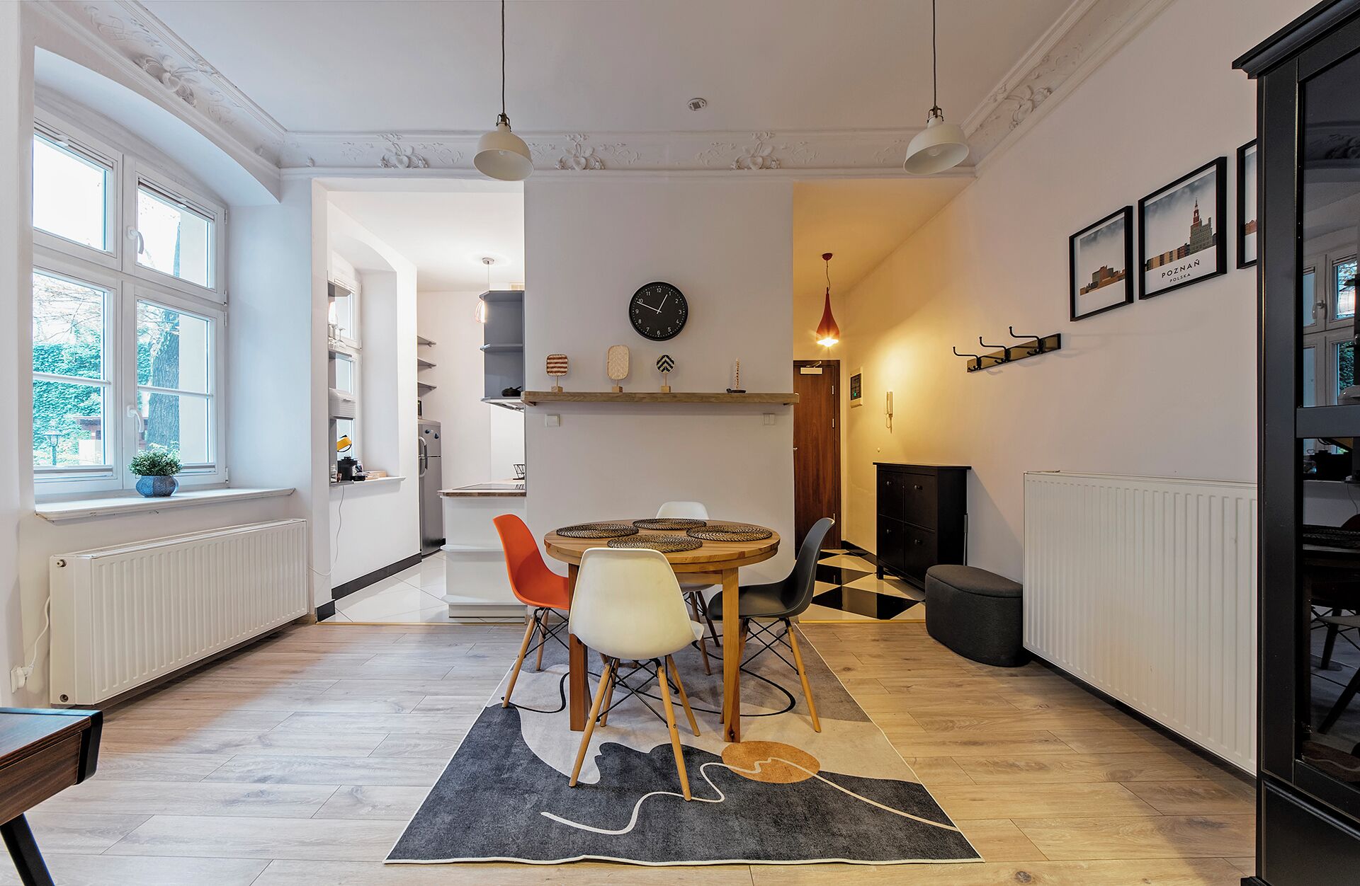 Une cuisine moderne avec une table à manger ronde, une horloge au mur et une vue sur l’extérieur grâce à de grandes fenêtres.