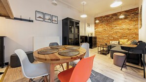 A modern living room with a brick wall, a dining area with a round wooden table, and a black cabinet. - RentPlanet - Wyspiańskiego (Poznań)