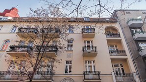A multi-story building with balconies, a central entrance with an ornate arch, and a clear sky. - RentPlanet - Wyspiańskiego (Poznań)