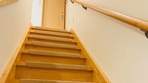 A wooden staircase with a handrail and carpeted steps leading to a door at the top. - Kamei House (Tokyo)