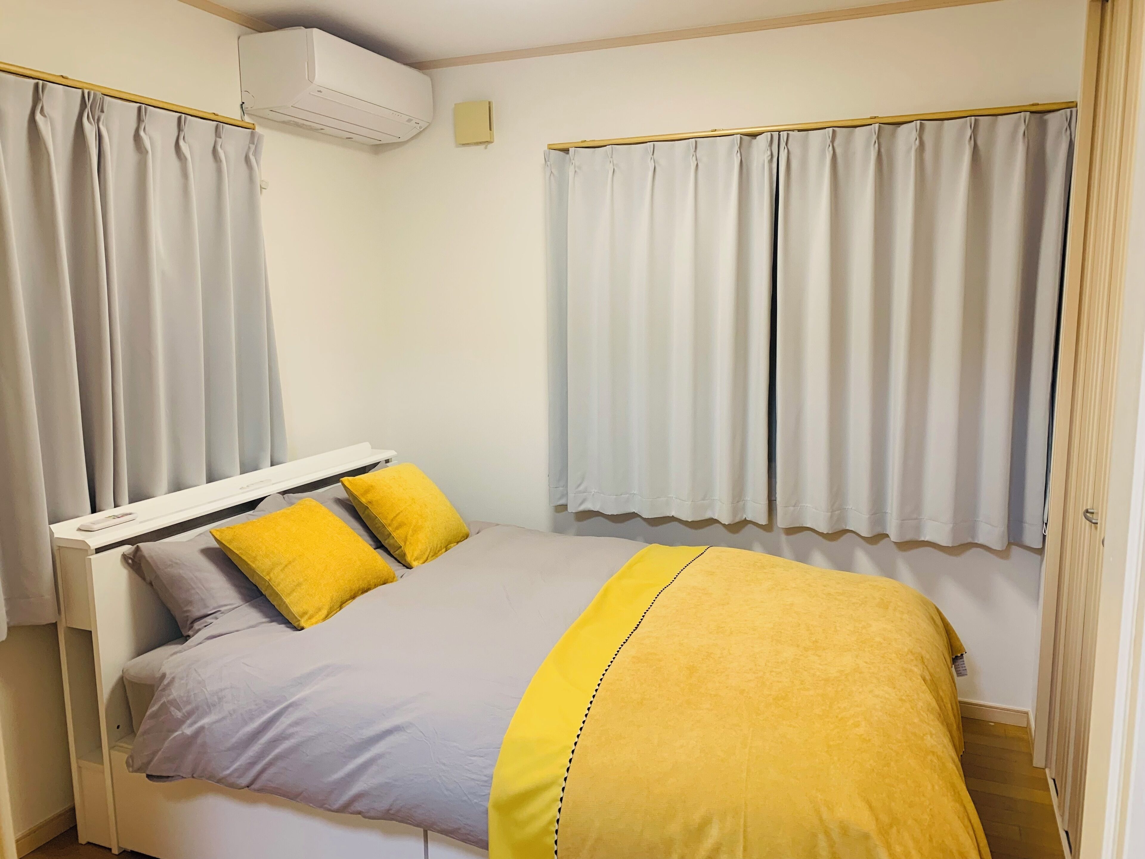 Une chambre à coucher comprenant un lit, des rideaux, un appareil de climatisation et une table de chevet.