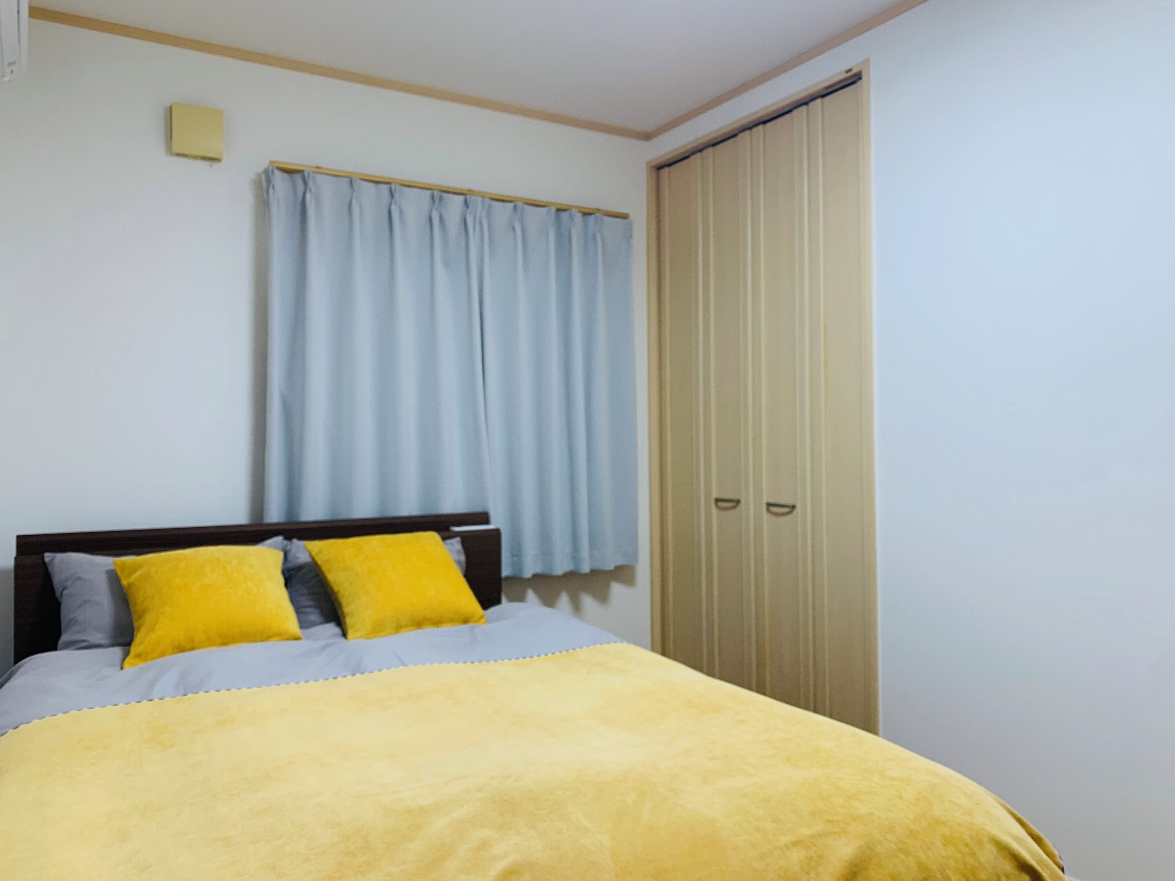 A bedroom with a bed, a window with curtains, and a wardrobe.