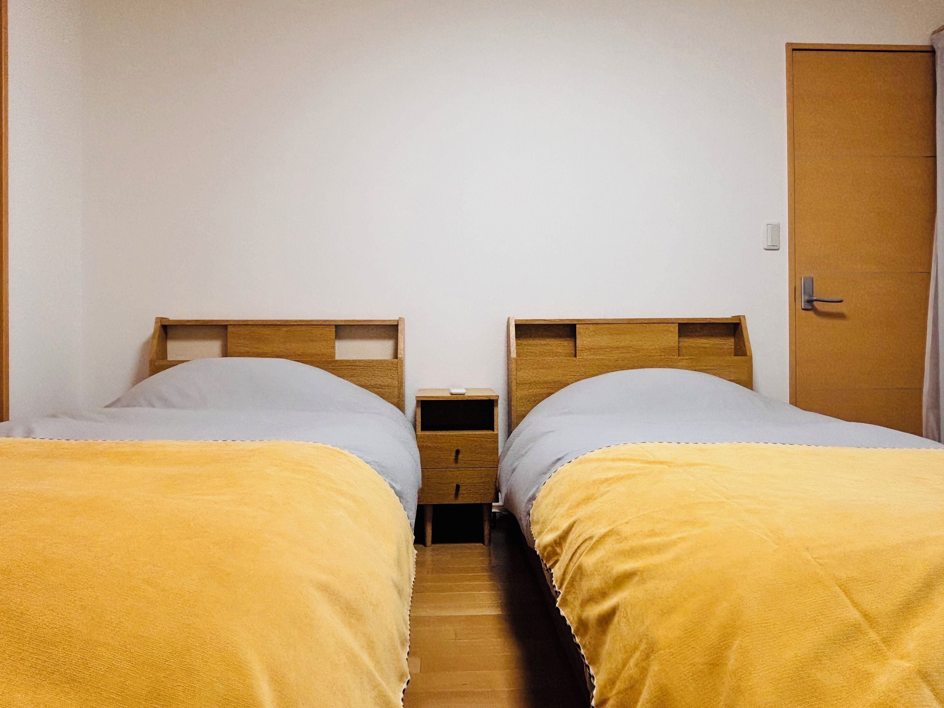 A twin room with two beds, wooden headboards, a small bedside table, and a door.