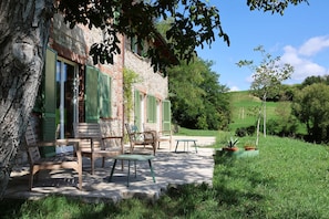 Ein Steinhaus mit grünen Fensterläden, Außenbereich zum Sitzen und einer grünen Landschaft.