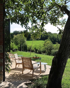 Ein Sitzbereich im Freien mit Holzkreisen und -tischen, umgeben von üppiger Bepflanzung und Blick auf eine grüne Wiese.
