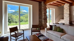 Ein Zimmer mit einer Steinsäule, einer Holzbalkendecke, einem Sofa, einem Sessel und einem Tisch mit Büchern.