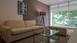 A modern living room with a sofa, a glass coffee table, a floor lamp, and a large window with a view of trees. - w Graceful 1BR With Balcony in Miraflores (Lima)