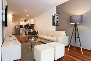A modern living room with a sofa, ottomans, a glass coffee table, and a floor lamp.