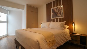 A neatly made bed with a beige blanket, a wooden headboard, a framed picture above the bed, and a bedside table with a lamp. - w Exceptional 2BR With Balcony in San Isidro (Lima)