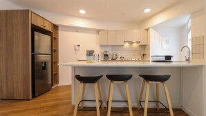 A modern kitchen with a built-in refrigerator, wooden cabinets, a white countertop, and two black bar stools. - w Exceptional 2BR With Balcony in San Isidro (Lima)