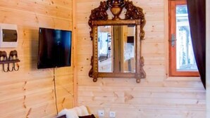 Puinen mökki, jonka sisustuksessa on sohva, televisio, peili ja ikkuna, jossa on verhot.