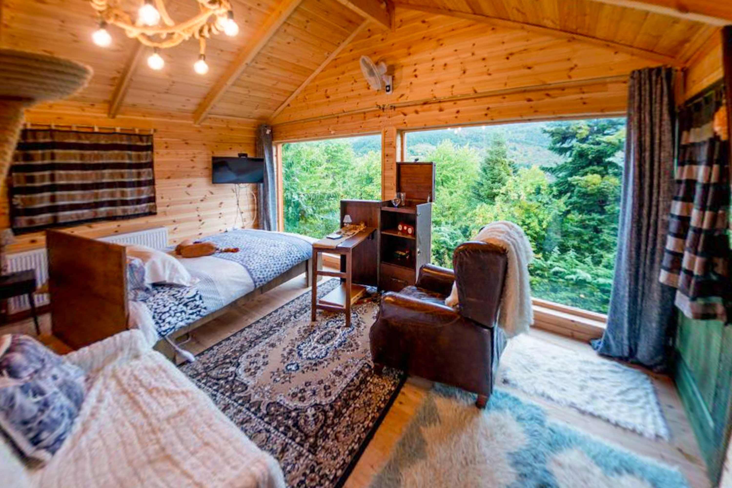 A cozy cabin room with a bed, a chair, a small table, and a television.